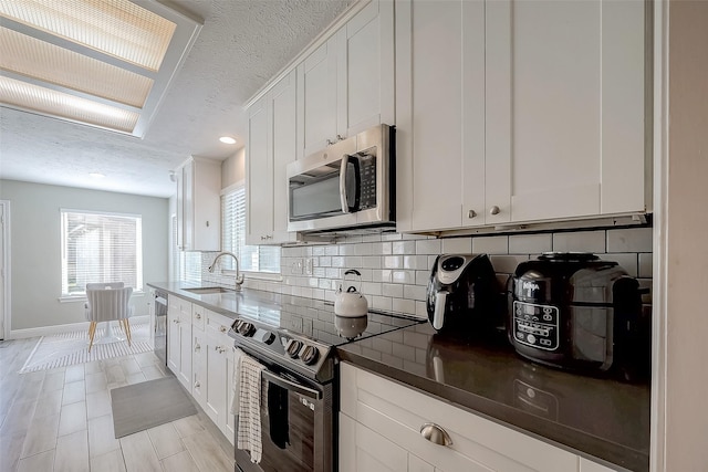 kitchen with backsplash, white cabinets, sink, a textured ceiling, and appliances with stainless steel finishes