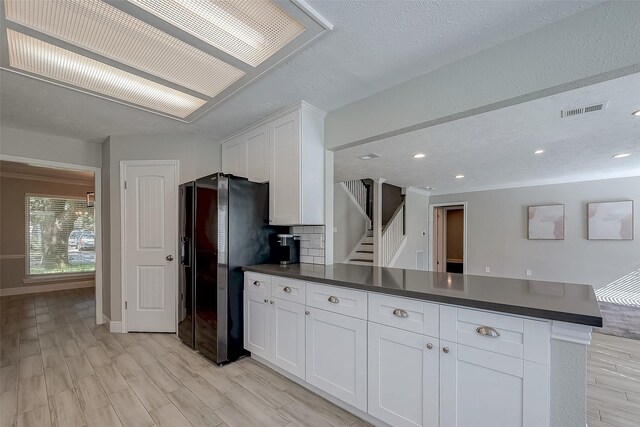 kitchen featuring backsplash, black refrigerator with ice dispenser, kitchen peninsula, a textured ceiling, and white cabinetry