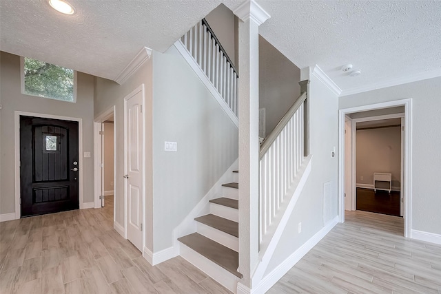 foyer with light hardwood / wood-style floors, ornamental molding, and a textured ceiling