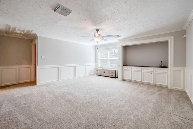 unfurnished living room with light carpet, ceiling fan, a textured ceiling, and ornamental molding