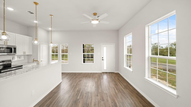 kitchen featuring white cabinets, appliances with stainless steel finishes, light stone countertops, and a wealth of natural light