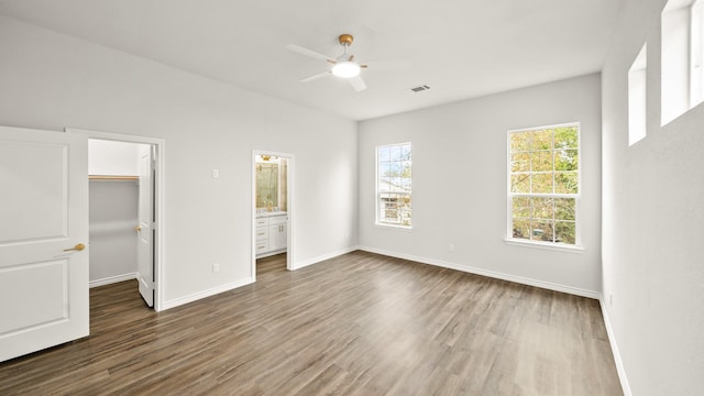 unfurnished bedroom featuring dark wood-type flooring, ensuite bathroom, ceiling fan, a spacious closet, and a closet