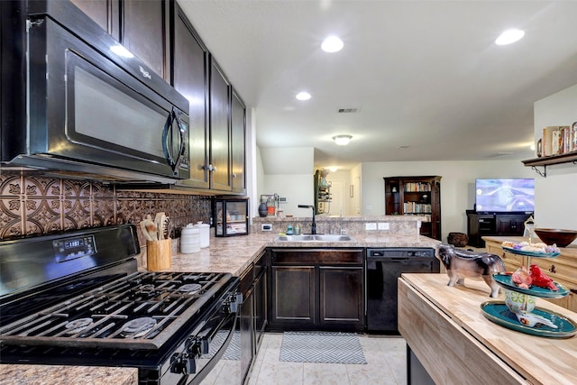 kitchen with kitchen peninsula, backsplash, light stone counters, sink, and black appliances