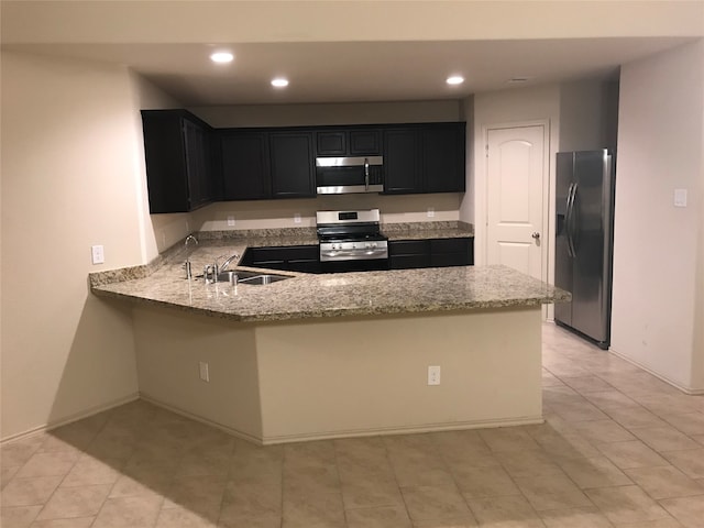 kitchen with kitchen peninsula, appliances with stainless steel finishes, light stone counters, and sink