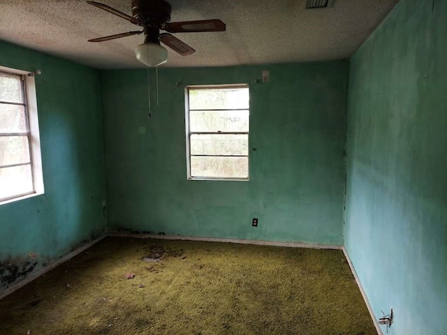 carpeted empty room with ceiling fan, a healthy amount of sunlight, and a textured ceiling