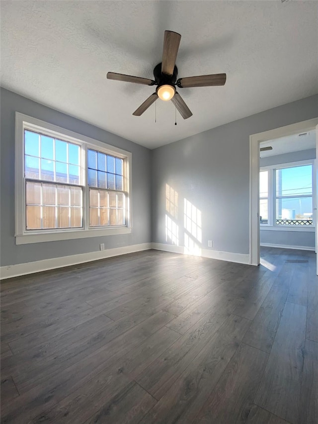 empty room featuring a wealth of natural light, ceiling fan, dark wood-type flooring, and a textured ceiling