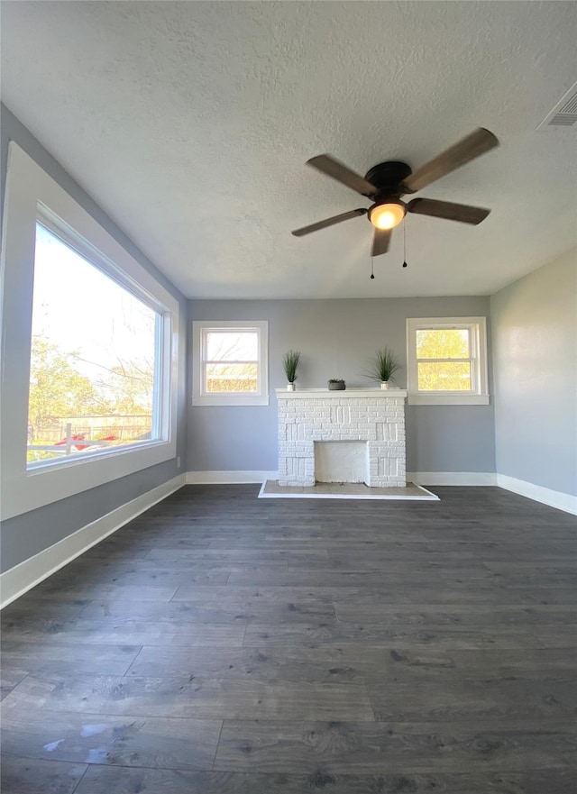 unfurnished living room with ceiling fan, dark wood-type flooring, a wealth of natural light, and a brick fireplace