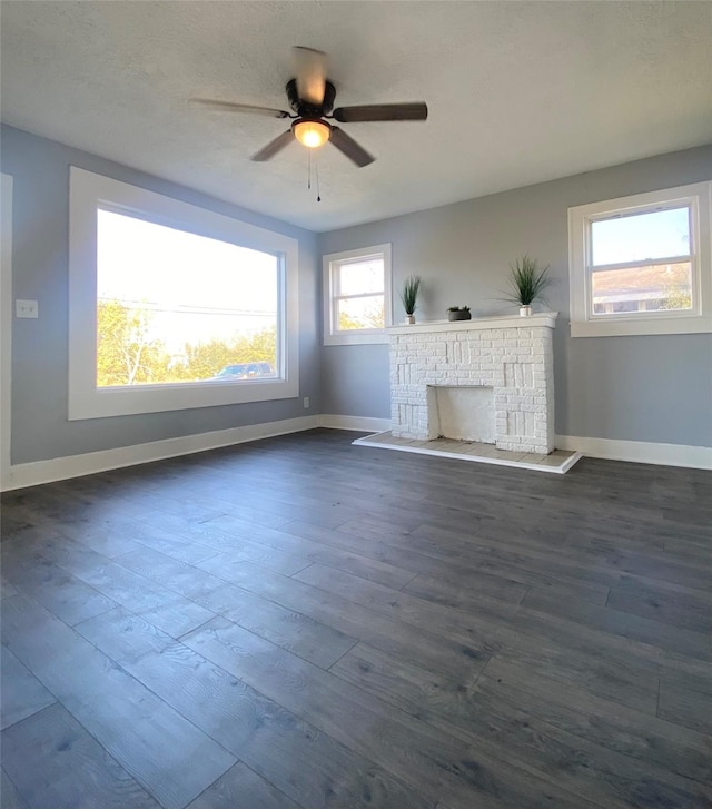 unfurnished living room with a fireplace, plenty of natural light, dark wood-type flooring, and ceiling fan