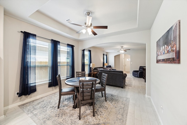 dining room with a raised ceiling, ceiling fan, and light wood-type flooring