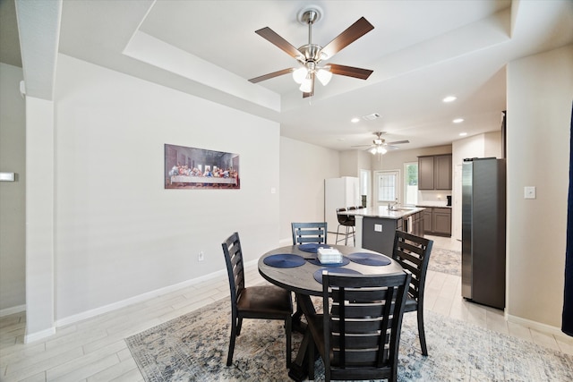 dining room featuring ceiling fan, light hardwood / wood-style floors, sink, and a tray ceiling