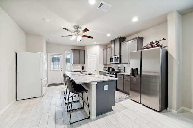 kitchen featuring light stone countertops, sink, stainless steel appliances, an island with sink, and a breakfast bar area