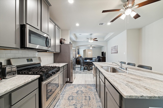 kitchen with sink, decorative backsplash, gray cabinets, light stone countertops, and stainless steel appliances