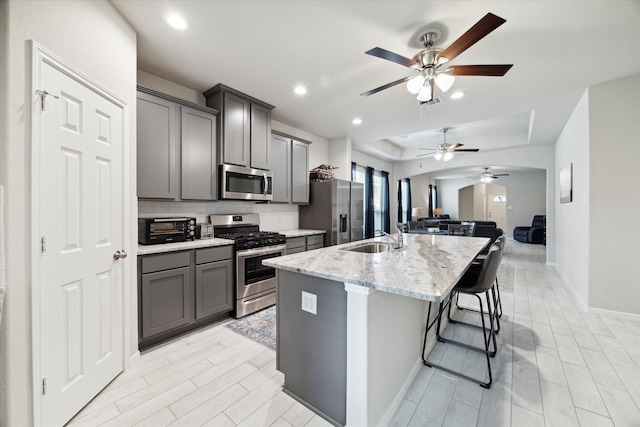 kitchen with gray cabinetry, sink, a kitchen breakfast bar, a center island with sink, and appliances with stainless steel finishes