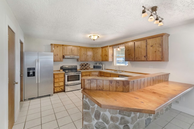 kitchen with sink, light tile patterned floors, a textured ceiling, kitchen peninsula, and stainless steel appliances