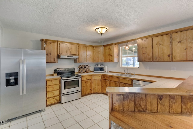 kitchen featuring sink, hanging light fixtures, a textured ceiling, light tile patterned floors, and appliances with stainless steel finishes