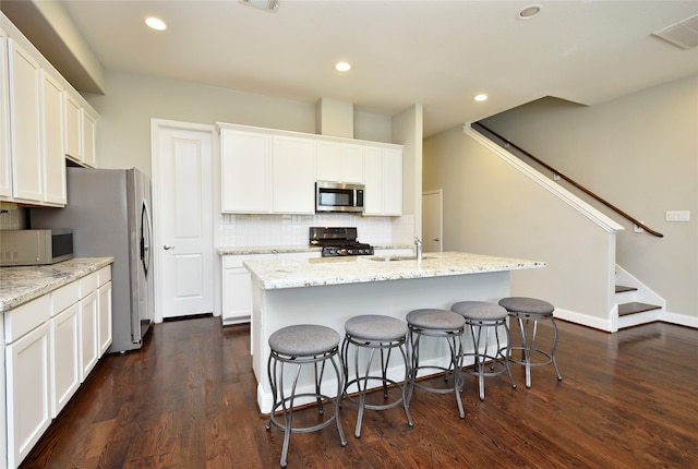 kitchen featuring light stone countertops, dark hardwood / wood-style flooring, black gas range oven, a center island with sink, and white cabinets