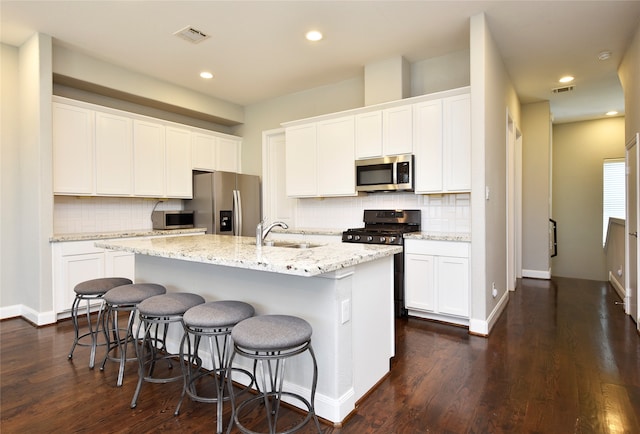 kitchen with dark wood-type flooring, sink, an island with sink, appliances with stainless steel finishes, and white cabinetry