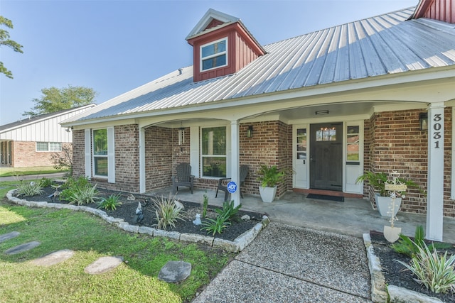 view of front facade with metal roof, a porch, and brick siding