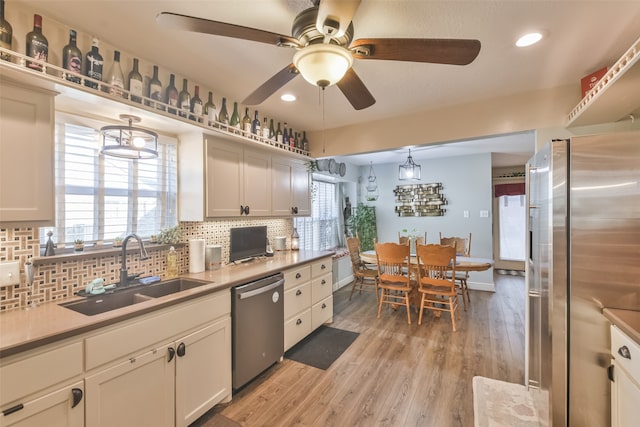 kitchen with white cabinetry, sink, light hardwood / wood-style floors, decorative light fixtures, and appliances with stainless steel finishes