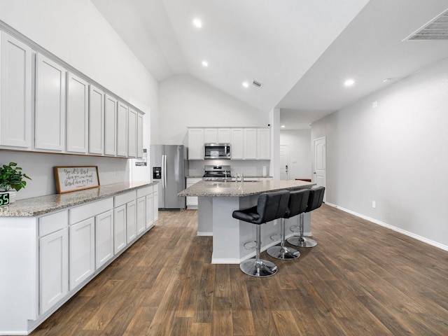 kitchen featuring appliances with stainless steel finishes, dark hardwood / wood-style flooring, a kitchen island with sink, and lofted ceiling