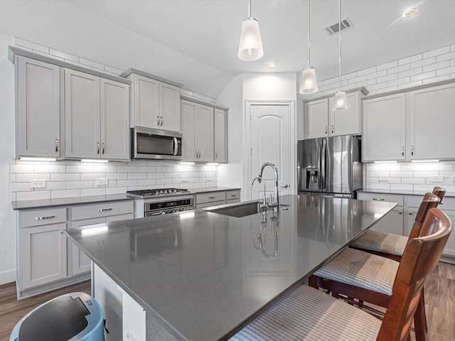 kitchen featuring appliances with stainless steel finishes, a center island with sink, hanging light fixtures, and sink