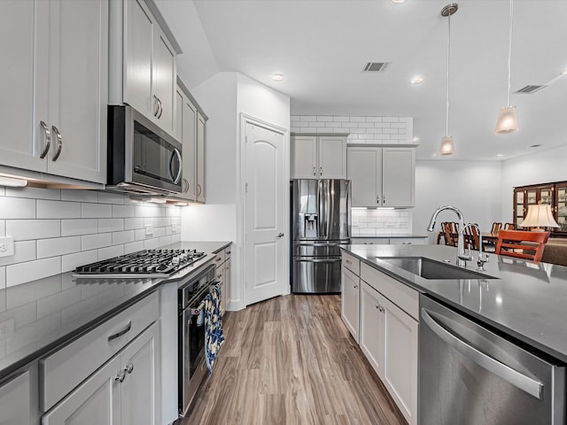 kitchen featuring backsplash, stainless steel appliances, sink, hardwood / wood-style flooring, and hanging light fixtures