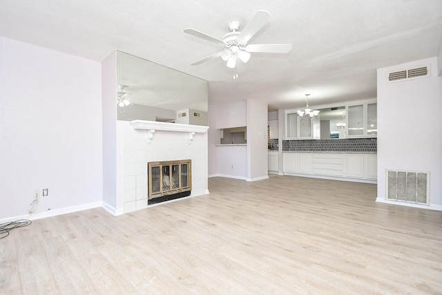 unfurnished living room with a textured ceiling, a tile fireplace, ceiling fan with notable chandelier, and light wood-type flooring