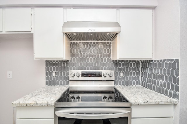 kitchen with light stone countertops, backsplash, stainless steel electric stove, wall chimney range hood, and white cabinetry