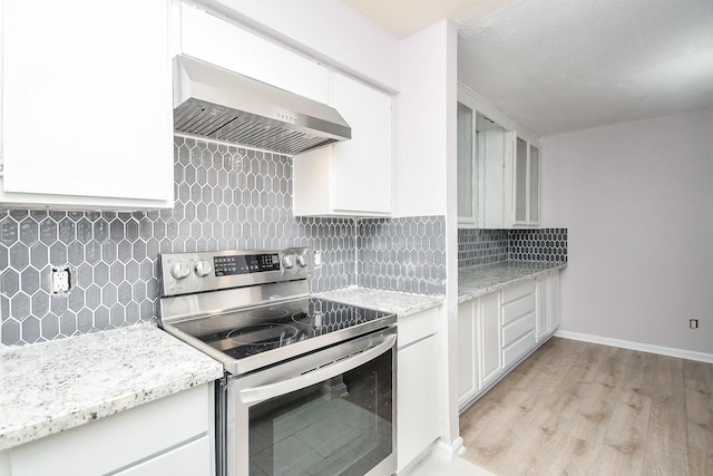 kitchen with stainless steel range with electric stovetop, wall chimney range hood, tasteful backsplash, light stone counters, and white cabinetry