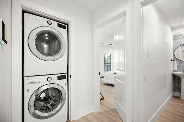 laundry area with stacked washing maching and dryer and light hardwood / wood-style floors