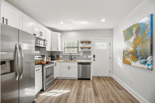 kitchen with backsplash, light hardwood / wood-style floors, sink, stainless steel appliances, and white cabinets