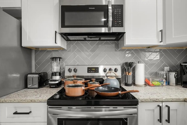 kitchen with decorative backsplash, white cabinets, appliances with stainless steel finishes, and light stone countertops