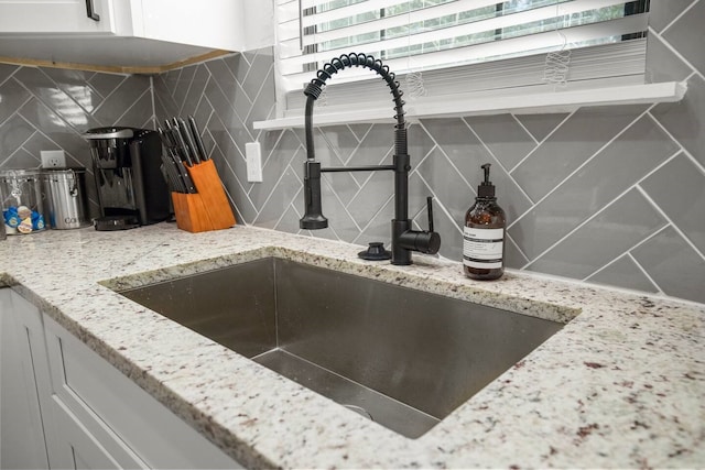 details with light stone countertops, sink, white cabinetry, and backsplash