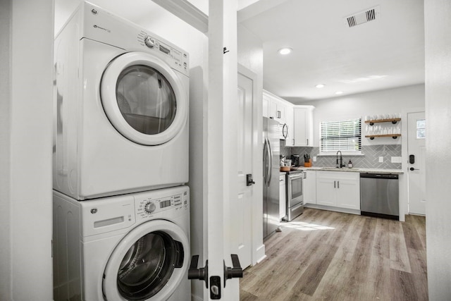 laundry area with light wood-type flooring, stacked washer and clothes dryer, and sink