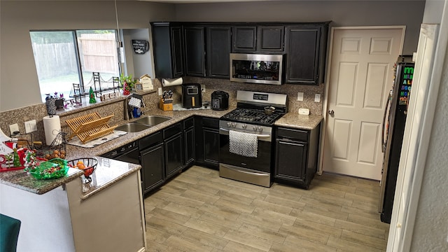 kitchen with light stone counters, sink, light wood-type flooring, and appliances with stainless steel finishes