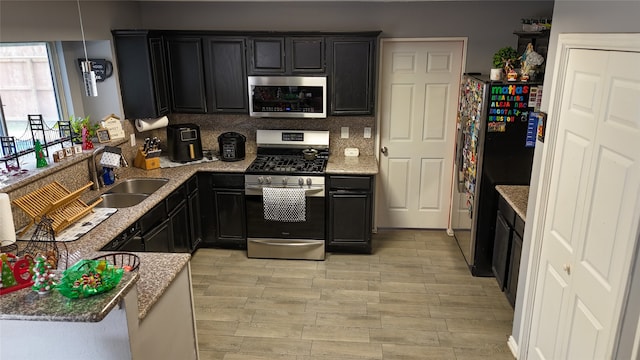 kitchen with light stone countertops, sink, backsplash, appliances with stainless steel finishes, and light wood-type flooring