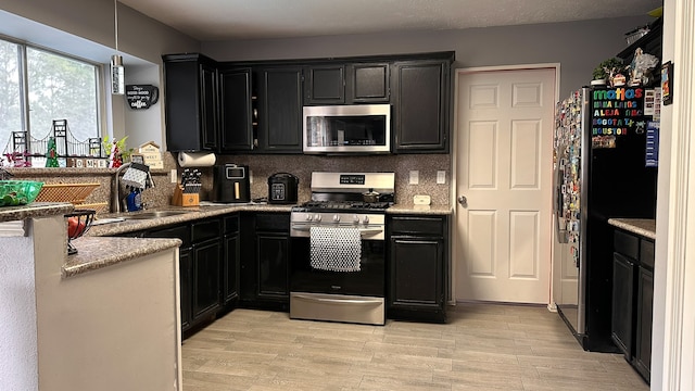 kitchen featuring light stone countertops, sink, light hardwood / wood-style floors, decorative backsplash, and appliances with stainless steel finishes