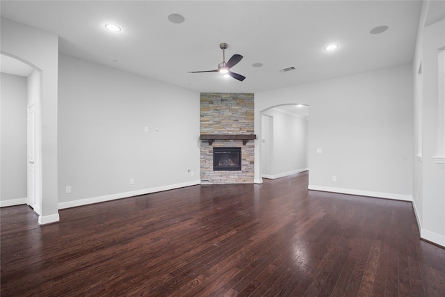 unfurnished living room featuring ceiling fan, a stone fireplace, and dark hardwood / wood-style flooring