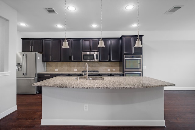 kitchen with decorative backsplash, hanging light fixtures, an island with sink, and stainless steel appliances