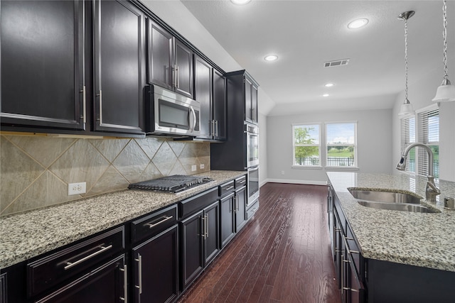 kitchen with appliances with stainless steel finishes, tasteful backsplash, dark wood-type flooring, sink, and hanging light fixtures