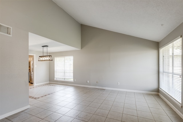 tiled empty room featuring a textured ceiling, vaulted ceiling, and a healthy amount of sunlight