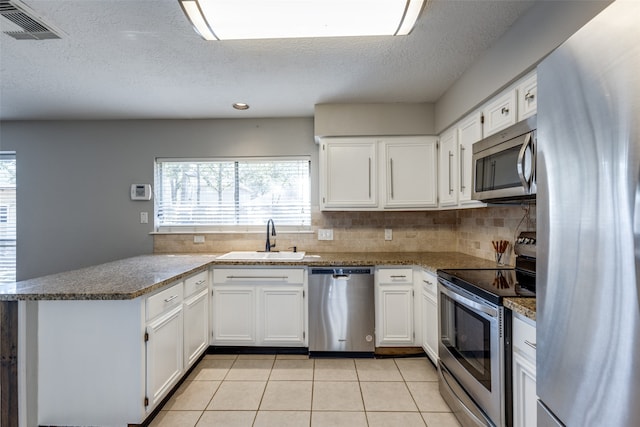 kitchen with white cabinets, sink, light tile patterned floors, appliances with stainless steel finishes, and kitchen peninsula