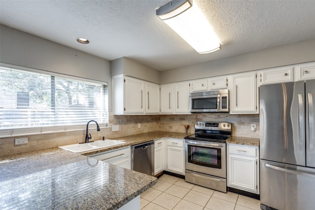 kitchen featuring white cabinets, stainless steel appliances, dark stone countertops, and sink