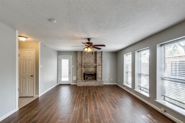 unfurnished living room featuring a textured ceiling, dark hardwood / wood-style flooring, a brick fireplace, and ceiling fan