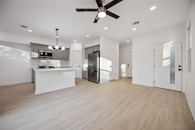 kitchen featuring decorative light fixtures, light hardwood / wood-style floors, an island with sink, and appliances with stainless steel finishes