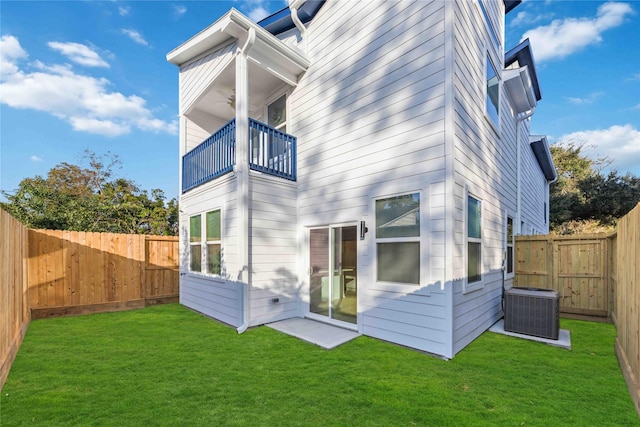 back of property featuring central AC unit, a balcony, a fenced backyard, a gate, and a yard