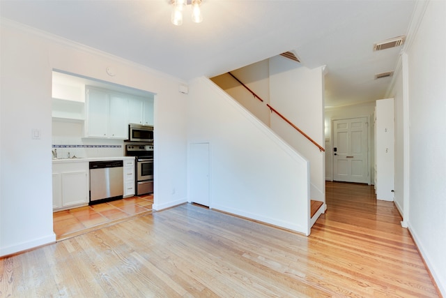 kitchen with white cabinetry, backsplash, light wood-type flooring, appliances with stainless steel finishes, and ornamental molding