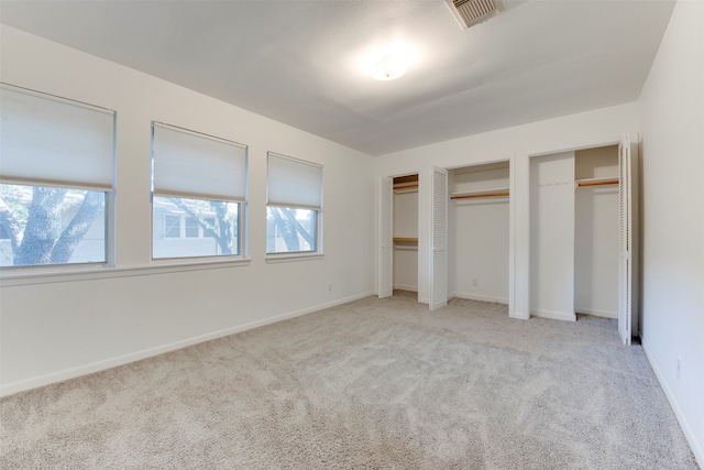 unfurnished bedroom featuring light carpet and multiple closets