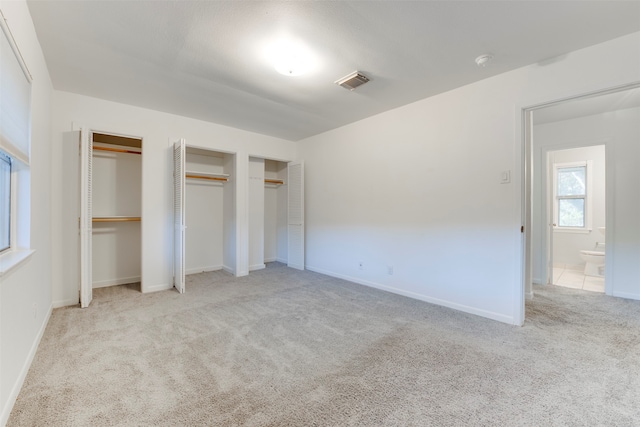 unfurnished bedroom featuring ensuite bath, light colored carpet, and two closets