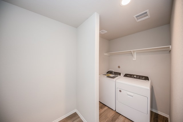 clothes washing area with washing machine and dryer and light wood-type flooring